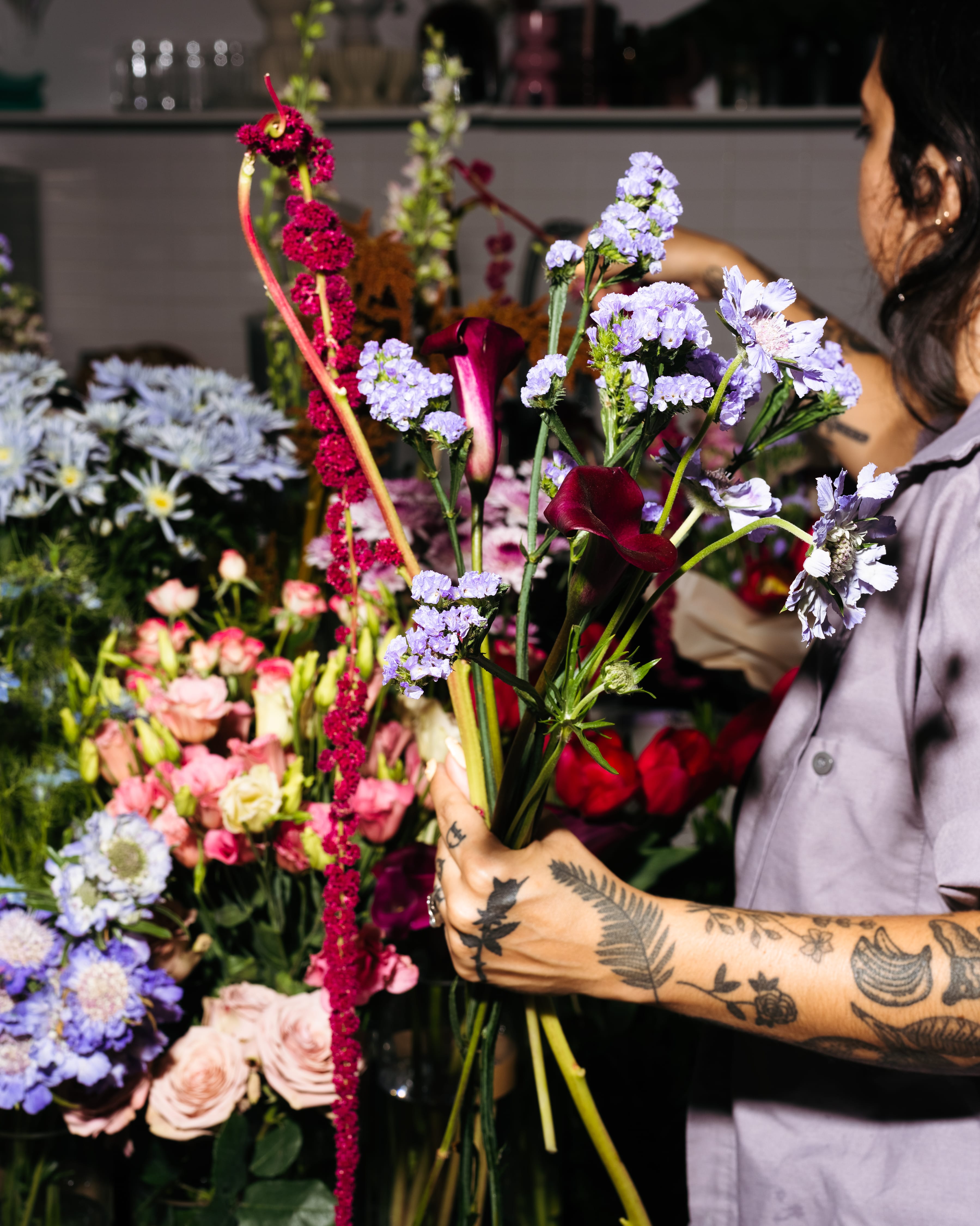 A person holds a bundle of flowers while reaching into containers to grab more in the process of making a bouquet.