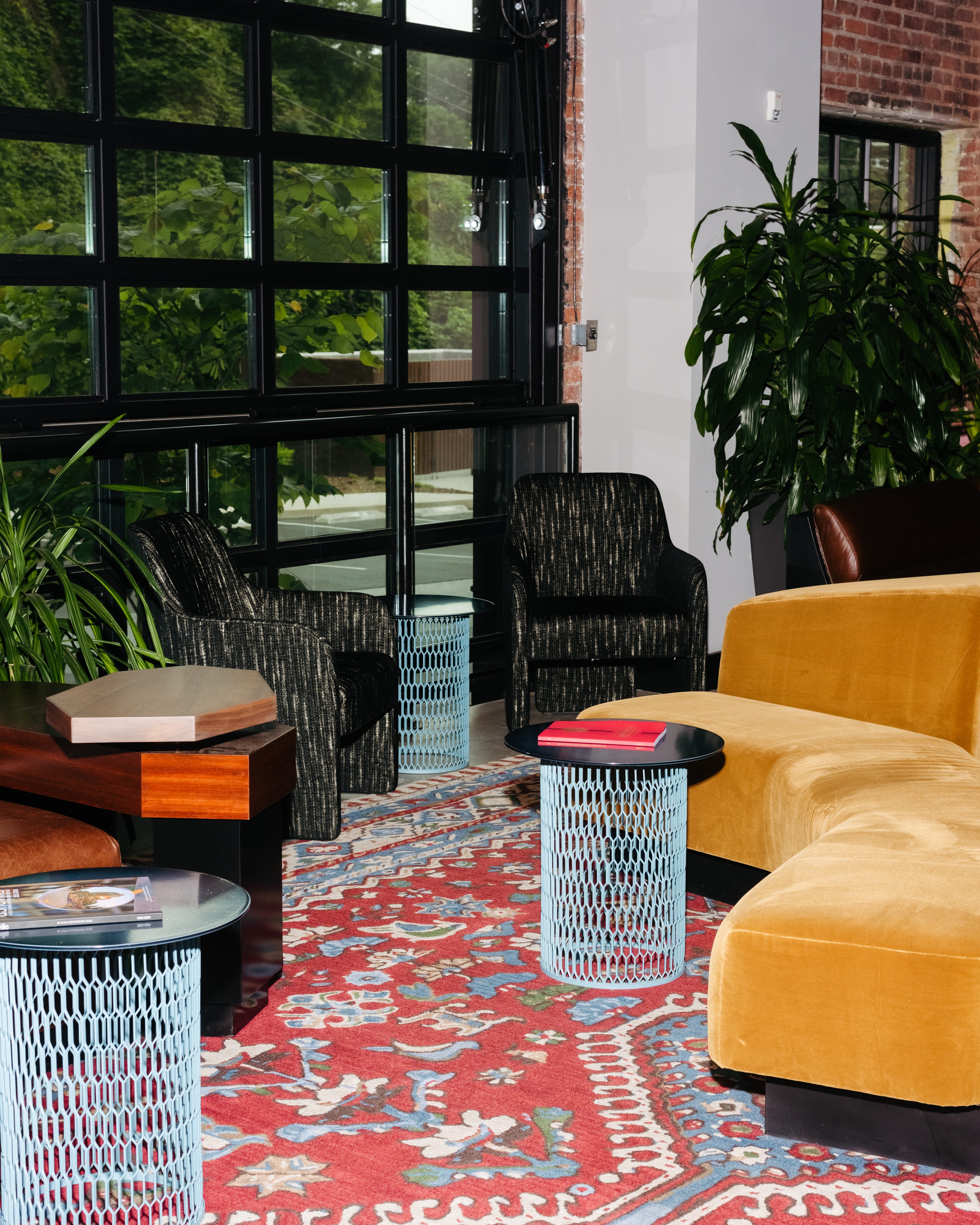 Chairs and yellow velvet sofas next to blue wire coffee tables in the lobby of a hotel